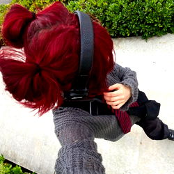 A young woman with red hair and headphones taking a selfie on a city street.