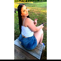 Pawg, a young woman posing on a bench with her hair in pigtails. She wears a white tank top and denim shorts.