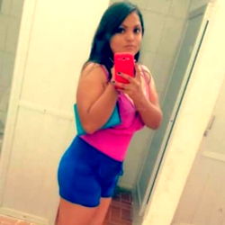 Andre Lop, a young adult female model taking a mirror selfie in a public restroom. She stands confidently, showcasing her outfit and phone.