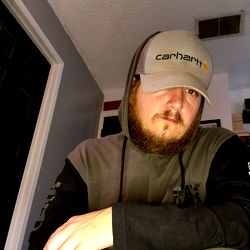 A person in a hoodie with a beard and a cap