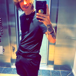 A young adult male with tattoos, taking a selfie in an elevator