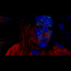 Thicc Anxiety: A model pose in a room with a blue light effect and a red background, showcasing a tattoo on the back of the neck.