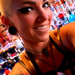 Tattooed woman with mohawk haircut and jewelry, in a bar setting, showcasing her unique style.