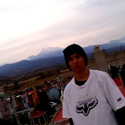 An individual in a baseball cap posing with a mountainous background
