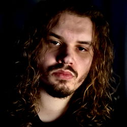 Contemplative Emo-style Photograph of a Man with Long Hair and Tattoos