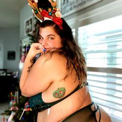 Model in a Christmas-themed outfit with reindeer ears and horns, posing at home for a holiday-themed photoshoot.