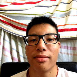 A young man with a unique hairstyle, sporting glasses and wearing a red lanyard.