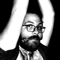 Jay, a beardy individual with a necklace, seems to be in mid-performance