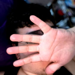 A person with a hand raised, partially blocking their face, appearing to be indoors.