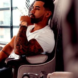 Myke, the Colombian OnlyFans model with tattoos, posing confidently in a luxurious chair.