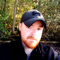 Bearded man with red hair and a cap in the woods.