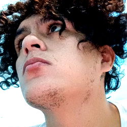 Young man with curly hair and pierced tongue, gazing off to the side.