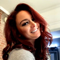 Tay, a radiant redhead with vibrant hair, is the focal point of this image. She's captured in mid-smile, her joyful expression radiating warmth.