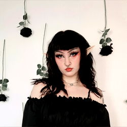 Elf Queen Stands Against Wall of Flowers