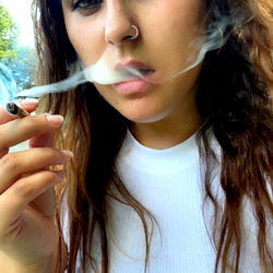 Ash, a young adult woman with her hair up, smoking and vaping