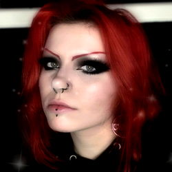 Red-haired individual with tattoos and piercings, possibly punk or emo aesthetic, looking directly at the camera.