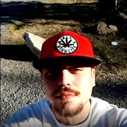 Ak-Saint, A Young Man with a Beard and Tattoo, Wearing a Red Baseball Cap and White Shirt