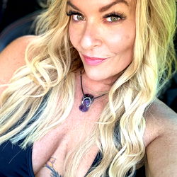 Annilovexxx in casual pose, with tattooed biceps and vibrant necklace