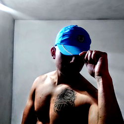 Alo, shirtless with blue baseball cap and tattoo, holding his hat
