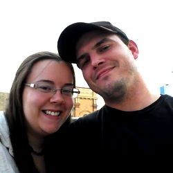 A couple posing for a photo in front of a building with a clock tower.